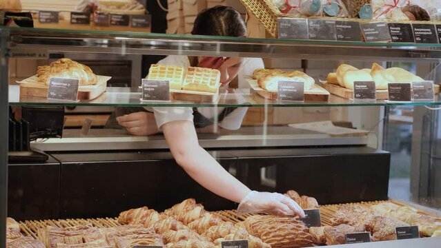 A saleswoman or owner of a bakery or pastry shop in uniform laying out pastries on the counter