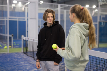 Portrait of two active teenage tennis players standing indoors discussing interesting topical...