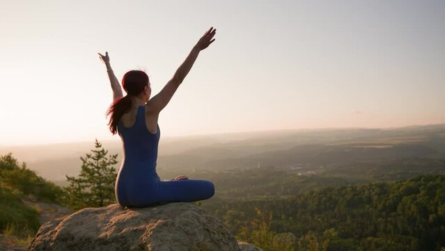 Athletic Woman Doing Yoga Poses on Top of a Mountain During Sunset. Sports Girl Trains and Does Stretching Exercises in the Mountains. Healthy Lifestyle, Zenism, Workout Concept. Slow Motion.