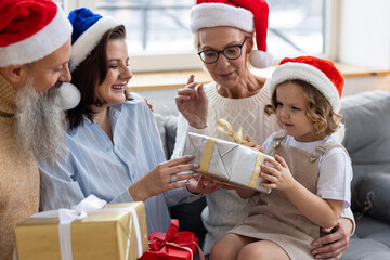 Fototapeta premium Grandmother, grandfather, daughter and granddaughter celebrating holidays at home together. Happy smiling family near beautiful Christmas new year tree exchanging gifts in the morning
