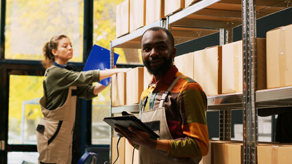 African american man using scanner in warehouse to scan barcodes on products stored in boxes. Male employee examining cargo merchandise on racks and shelves, reviewing logistics.