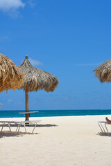 Beautiful view of beach with white sand, sun loungers and rustic palapa  against backdrop of azure...