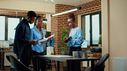 Department staff checking data analytics on tablet, examining business reports on papers. Company employees reading presentation notes to create new executive project in boardroom meeting.