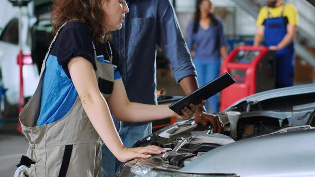 Mechanic in car service uses tablet to calculate invoice after fixing broken automobile engine. Auto repair shop worker uses device to inform man of final costs after repairing vehicle, close up