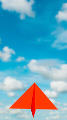 Blue sky with clouds where a red paper plane flies, theme of leadership and achieving goals