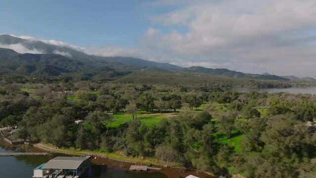 Fly along lake bank with marina and boat rental. Campground on peninsula on sunny day. Cachuma Lake, California, USA