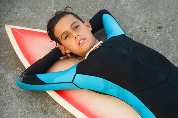 Preteen surfer boy in a wet suit lying on his surfboard at the beach