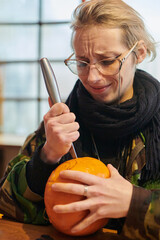 A modern blonde woman in military uniform is carving spooky pumpkins with a knife for Halloween...