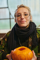 A modern blonde woman in military uniform is carving spooky pumpkins with a knife for Halloween...