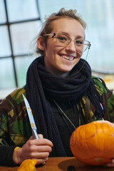 A modern blonde woman in military uniform is carving spooky pumpkins with a knife for Halloween...