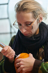 A modern blonde woman in military uniform is carving spooky pumpkins with a knife for Halloween...