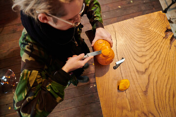 A modern blonde woman in military uniform is carving spooky pumpkins with a knife for Halloween...