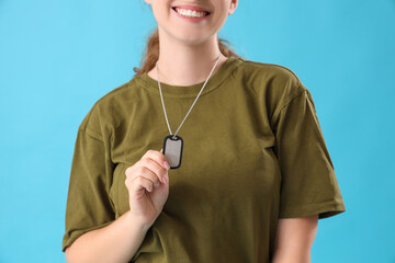 Young female soldier with military tag on light blue background