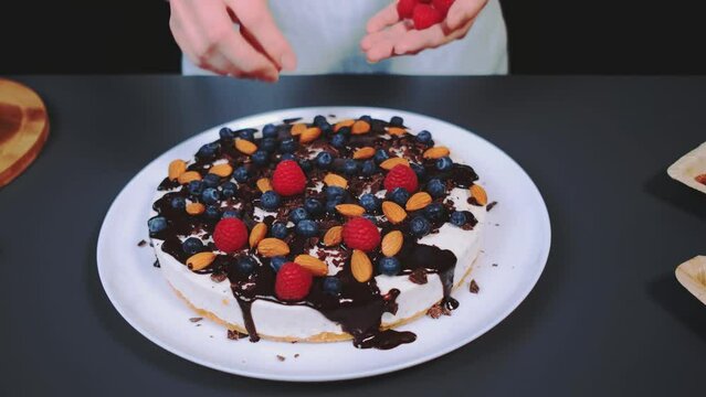 Woman decorating stracciatella cake with fresh raspberries. Close-up of a table. Cooking in the kitchen.