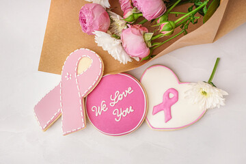 Pink cookies with ribbon, text WE LOVE YOU and bouquet of flowers on white grunge background. Breast cancer awareness concept