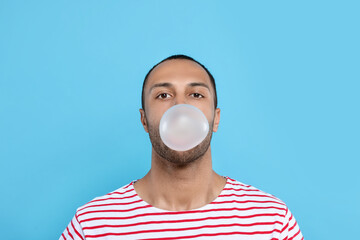 Portrait of young man blowing bubble gum on light blue background