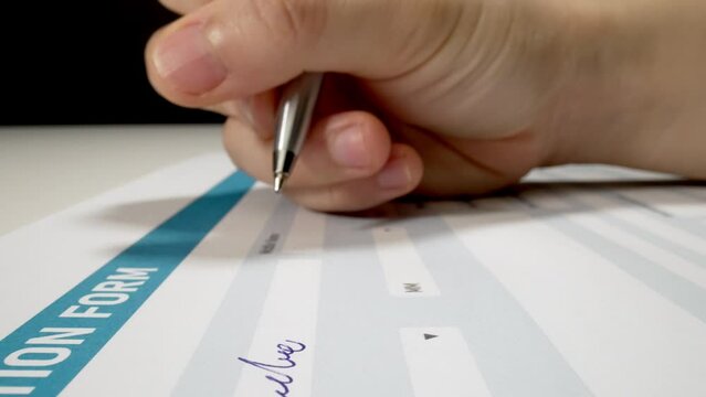 Closeup macro shot movement of applicant's hand filling personal information and writing name on job application form document. Employment and job opportunity for unemployed candidate.