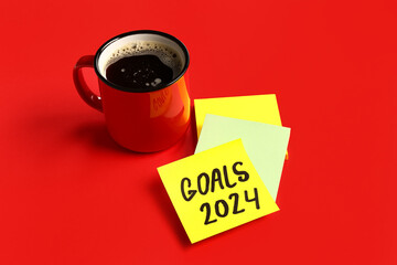 Sticky notes with goals for 2024 and cup of coffee on red background