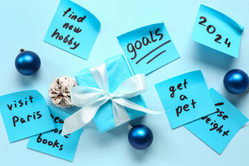 Sticky notes with goals for 2024, gift box and Christmas balls on blue background