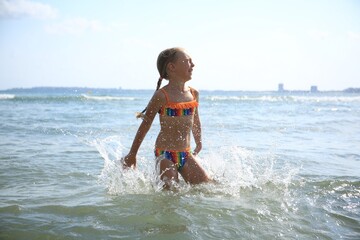 Emotional little girl having fun in sea on sunny day. Beach holiday