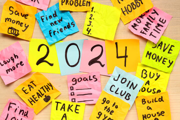 Sticky notes with different goals for 2024 on beige wooden background