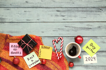 Sticky notes with different goals for 2024, gift box, cup of coffee and Christmas decorations on grey wooden background