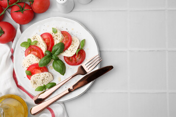 Caprese salad with tomatoes, mozzarella, basil and spices served on white tiled table, flat lay. Space for text