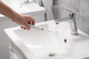 Man holding electric toothbrush under flowing water above sink in bathroom, closeup