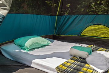 Close up view of a mattress, cushion, sheet and towels inside a tent in the forest