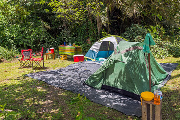 Camp site in tropical forest, two tents, chairs, table, food and drinks, cooler, soap and towel