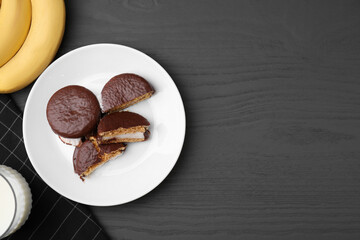 Tasty sweet choco pies, bananas and glass of milk on grey wooden table, flat lay. Space for text