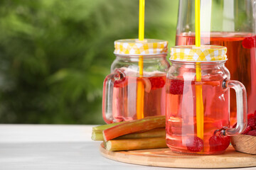 Tasty rhubarb cocktail with raspberry and stalks on white wooden table outdoors, space for text