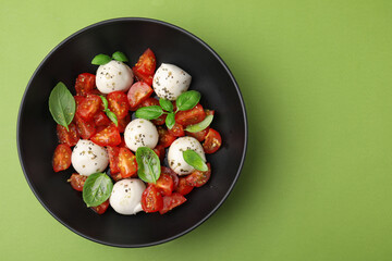 Tasty salad Caprese with tomatoes, mozzarella balls and basil on green background, top view. Space for text