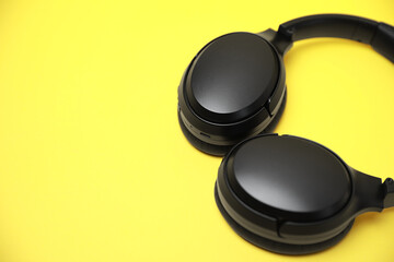 Modern wireless headphones on yellow background, closeup. Space for text