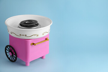 Portable candy cotton machine on light blue background, space for text