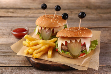 Cute monster burgers served with french fries and ketchup on wooden table. Halloween party food