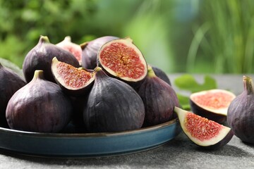 Whole and cut ripe figs on light grey textured table against blurred green background, closeup