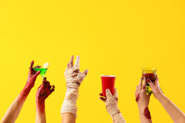 Zombie and mummy hands with drinks on yellow background. Halloween celebration