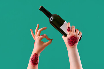 Zombie hands holding bottle of wine and showing OK gesture on green background. Halloween...
