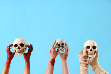 Zombie and mummy hands holding skulls on blue background. Halloween celebration