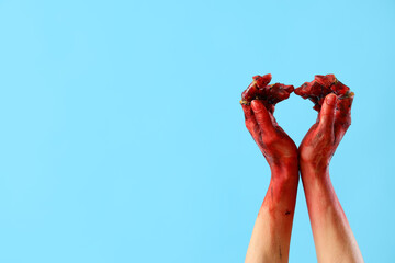 Bloodstained zombie hands making heart on blue background. Halloween celebration