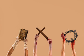 Zombie hands holding old book, wooden cross and crown of thorns on beige background. Halloween...