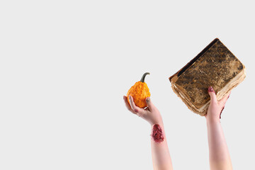 Zombie hands holding pumpkin and old book on white background. Halloween celebration