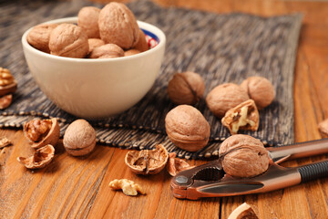 Bowl with walnuts and nutcracker on wooden background