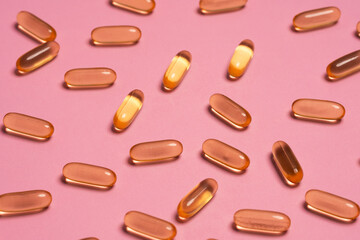 Top view composition of orange vitamin pills scattered on pink background in light studio