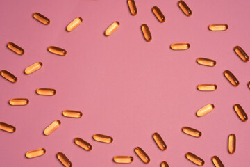 Top view frame of orange vitamin pills scattered on pink background in light studio. Frame of pills