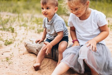 A little boy and a little girl are sitting on a log with their feet in the sand on a summer day in a forest