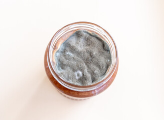 Open jar with sweet jam and mold on a white background. Mold in a jar of raspberry jam. Hazardous to health.  - obrazy, fototapety, plakaty