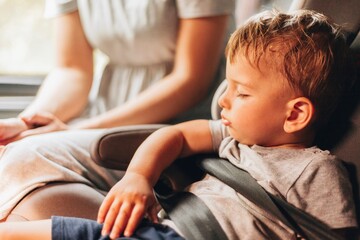 An adorable little toddler baby boy fell asleep in a car seat on a bus ride