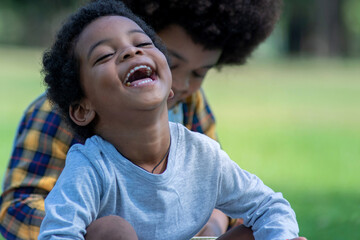 African little boy laughing happily sitting in group of friends in park